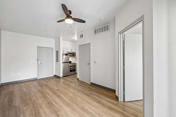 A room with a ceiling fan and a kitchen area in the background.