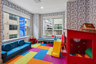A colorful children's playroom with a blue sofa, a yellow slide, and a red playhouse.