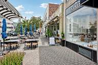 A street view of a cafe with tables and chairs and umbrellas.