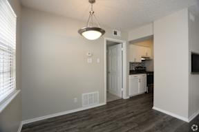 A room with a light hanging from the ceiling and a doorway leading to a kitchen.