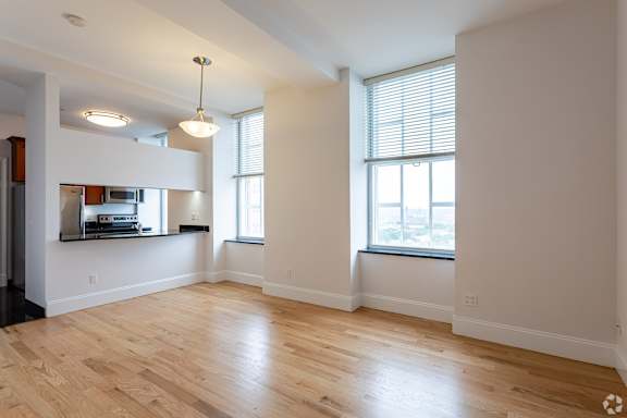 A large empty room with wooden floors and a window with blinds.