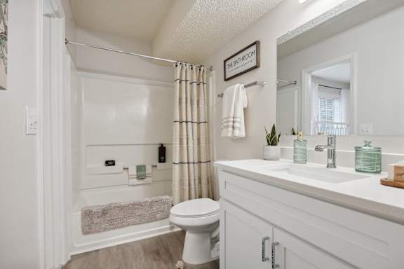 A white bathroom with a toilet, sink, and shower at St. Andrews Reserve Apartments in Wilmington, NC