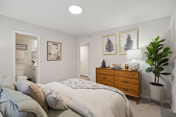 A bedroom with a bed, dresser, and two framed pictures on the wall at St. Andrews Reserve Apartments in Wilmington, NC