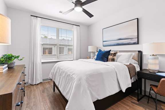 A bedroom with a bed, a desk, and a ceiling fan.