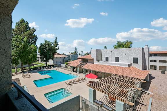 A large outdoor swimming pool with a red umbrella and lounge chairs.