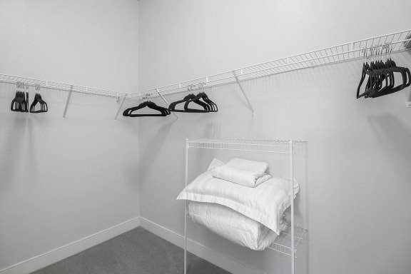 a walk in closet with a rack of folded white towels and hangers with shoes