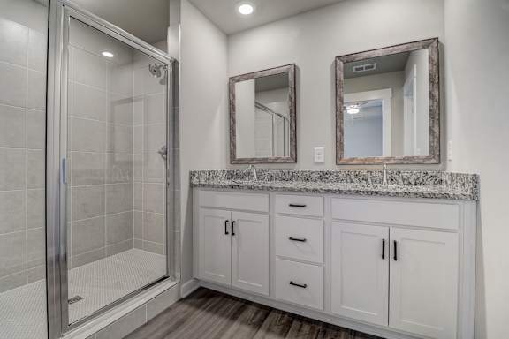 A bathroom with a walk-in shower, marble countertop, and two mirrors.