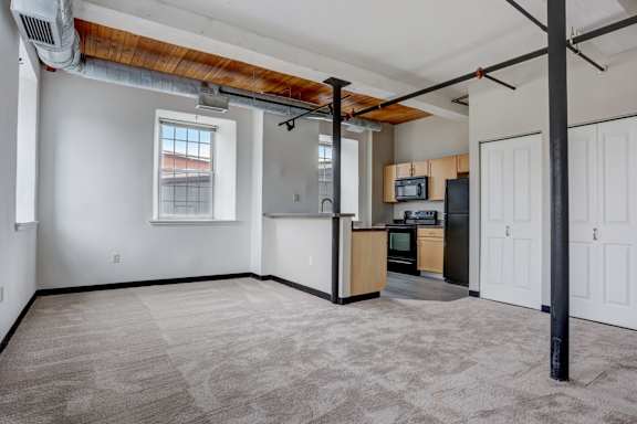an empty living room with a kitchen in the corner