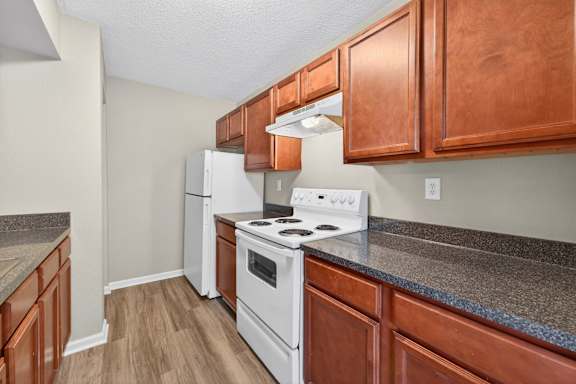 A kitchen with a white stove top oven and white refrigerator.
