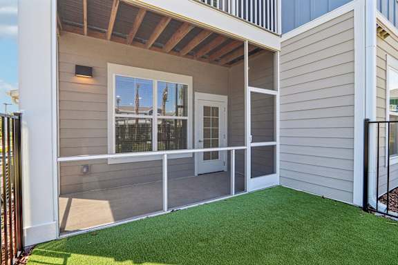 A balcony with a glass door and a window overlooking a green lawn.