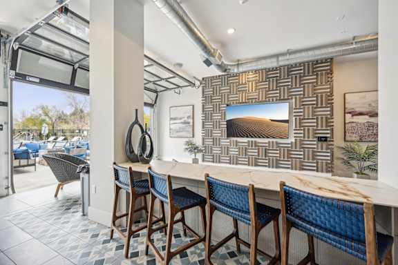 a long bar with blue chairs and a wall with a television at The Quarry Luxury Apartment Homes, Fort Collins, 80526