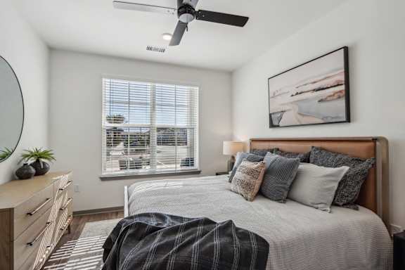 A bedroom with a large bed, a ceiling fan, and a window with blinds at The Pullman Luxury Apartment Homes, Georgia
