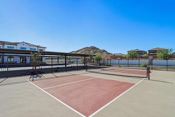 A tennis court is surrounded by a fence and a building.