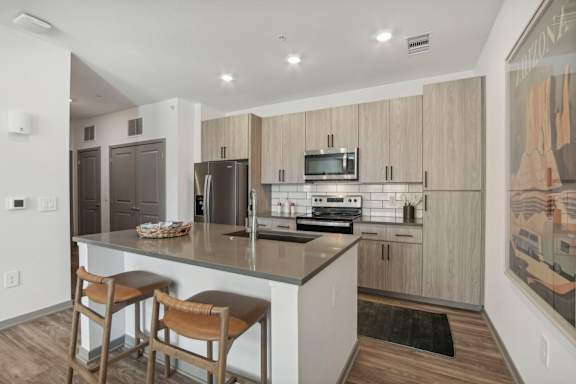 a kitchen with a large island with two stools in front of a counter top at The Maddox Luxury Apartment Homes, Arizona, 85326