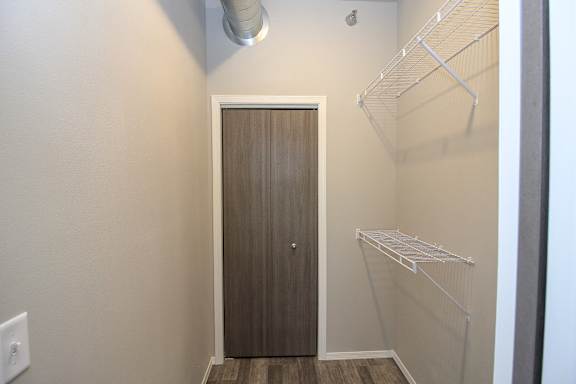 A white closet with a brown door and a white shelf.