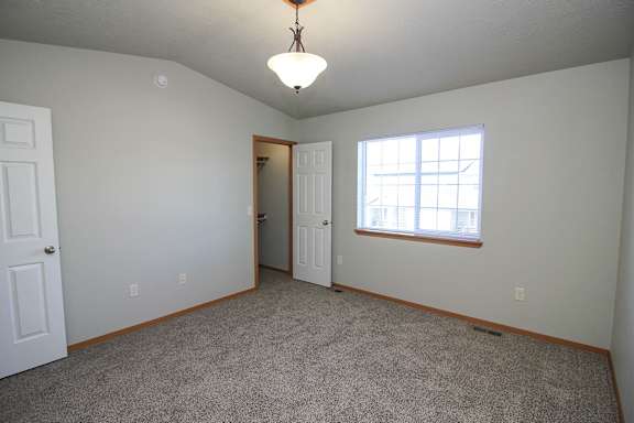 A room with a carpeted floor, a ceiling light, and a window with blinds.