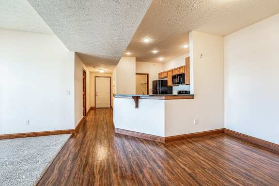 the living room and kitchen of an empty apartment with wood flooring and white walls