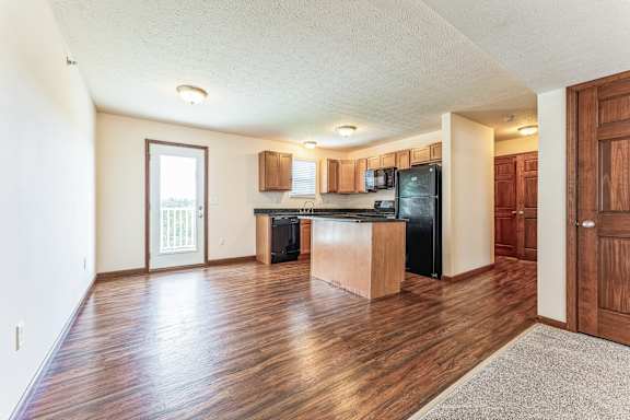 an empty living room with a kitchen and a door to a balcony