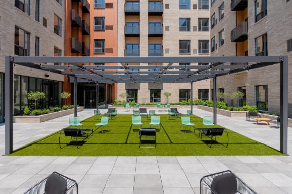 an outdoor lounge area with lounge chairs on a lawn in front of an apartment building at TREO Apartments, Cleveland, 44116