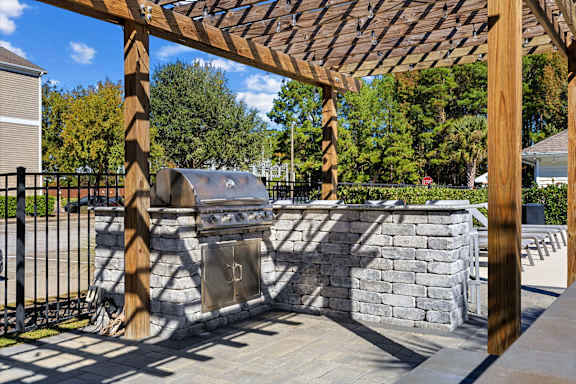 A wooden pergola over a stone wall with a trash can underneath.