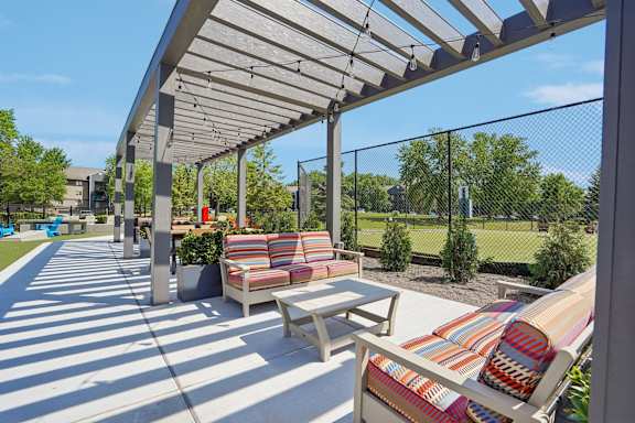 A sunny day at the park with a striped couch and a bench under a canopy.