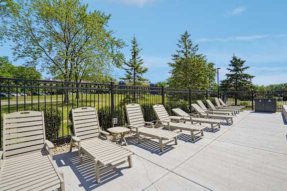 A row of wooden lounge chairs are arranged on a concrete patio.