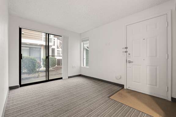A room with a carpeted floor, a white door, and a sliding glass door leading to a balcony. at AVIA Lofts on Parkway, Vancouver, WA 98662