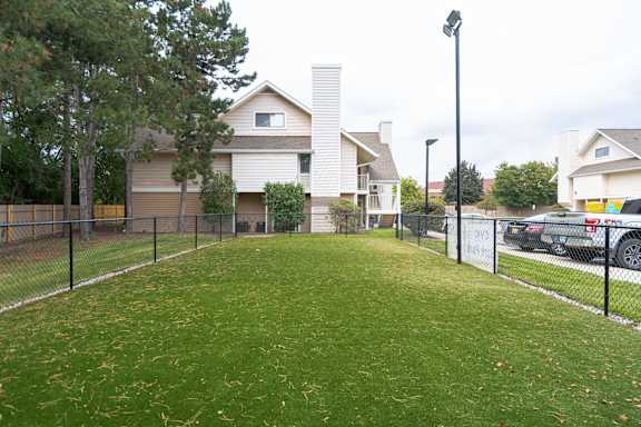 A grassy area in front of a house with a fence and a car parked in the background. at AVIA Lofts on Victors Way, Ann Arbor, MI 48108