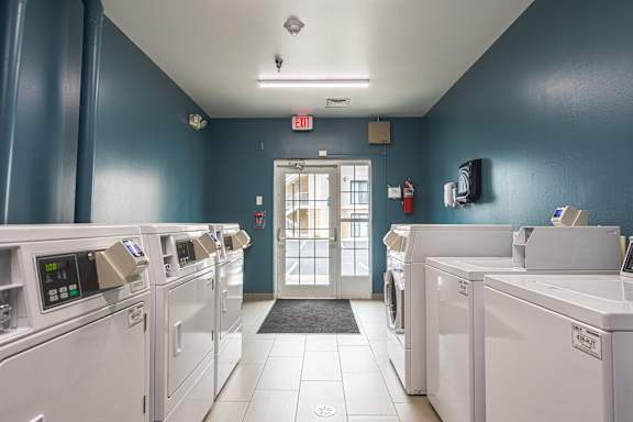 A laundromat with washers and dryers and a red exit sign. at AVIA Lofts on Victors Way, Ann Arbor Michigan