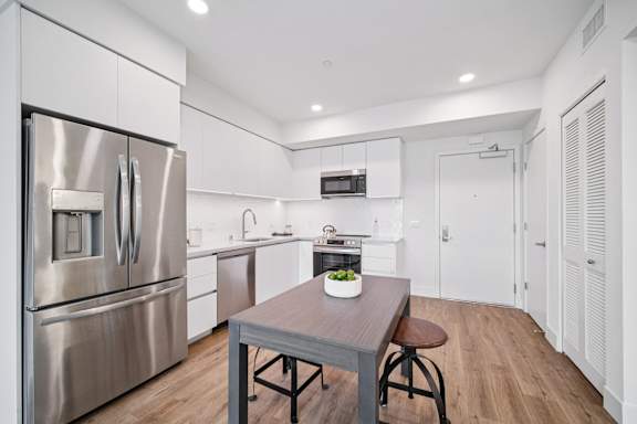 A modern kitchen with a stainless steel refrigerator and a wooden table with a bowl of fruit on it.