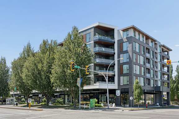 A modern multi-story building with balconies is situated on a street corner with a traffic light.