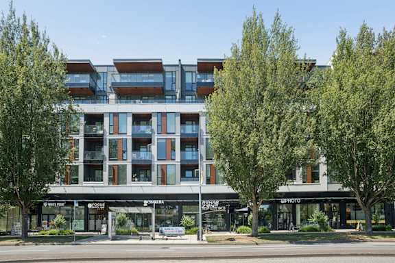 A modern building with a glass facade and trees in front.