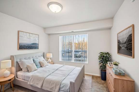 A bedroom with a large bed, a nightstand, and a window with blinds.