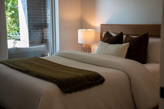 A bed with a white comforter and a green throw.