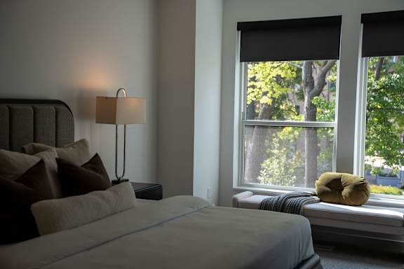A bedroom with a bed, pillows, a lamp, and a window with a view of trees.