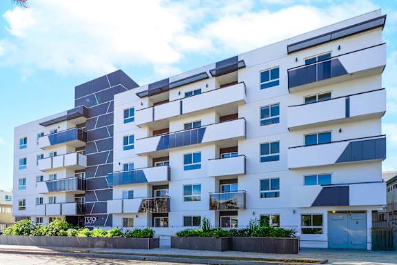 A modern apartment building with balconies and a blue sky in the background.