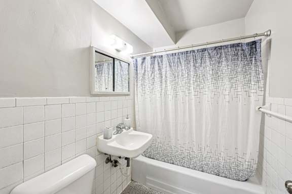 A white bathroom with a white tub, sink, and shower curtain.