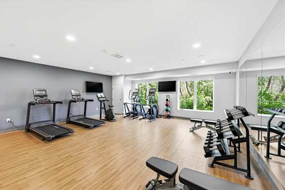 A well-lit gym with treadmills, exercise bikes, and weight benches.