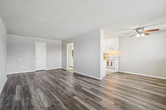 A room with a ceiling fan and a kitchenette in the background.