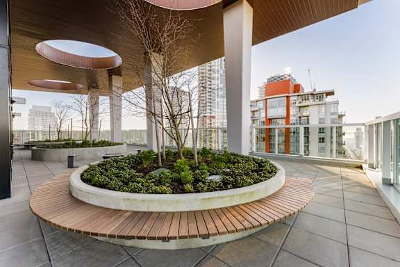 A modern outdoor seating area with a circular wooden table surrounded by plants.