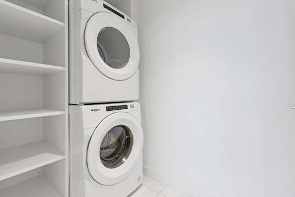 A white washing machine is placed in a white laundry room.