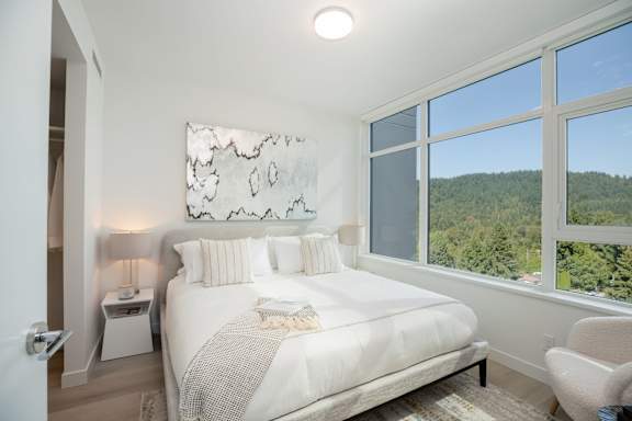 A bedroom with a large bed and a view of the forest outside the window.