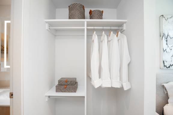 White shelves with clothes hanging and boxes on them.