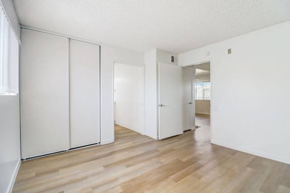 A room with white walls and wooden flooring with a white door and a white wardrobe.
