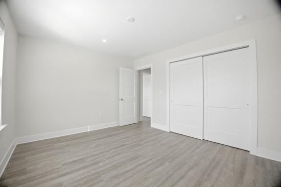 A room with white walls and wooden flooring with a white door and two white closet doors.