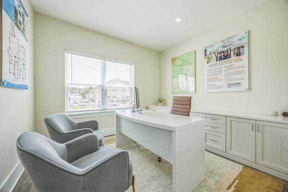 A room with a desk, chairs and posters on the wall.