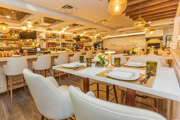 A restaurant with white tables and chairs and a bar area in the background. at Palma, Florida, 33166