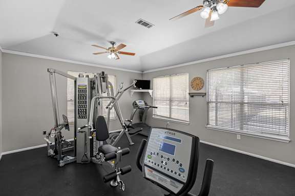 A home gym with a variety of equipment including a treadmill, weights, and a monitor.