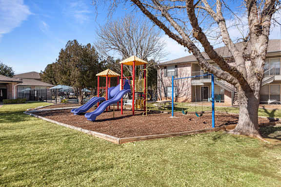 A playground with a yellow and blue slide and a red and blue swing set.