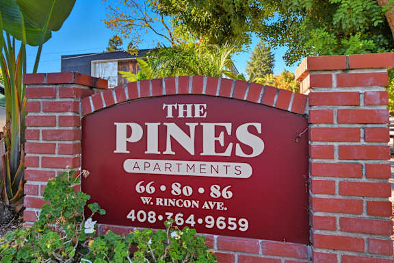 A sign for The Pines Apartments is shown in front of a green plant.